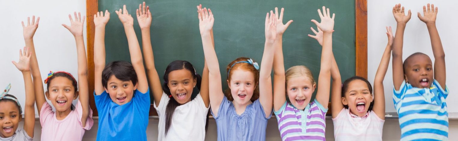 acht kleine Kinder stehen vor Tafel und halten ihre Arme in die Luft