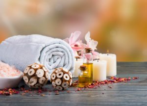 Wellnessfoto mit zusammengerolltem Handtuch, Ölen, Kerzen, Meersalz und Blumen