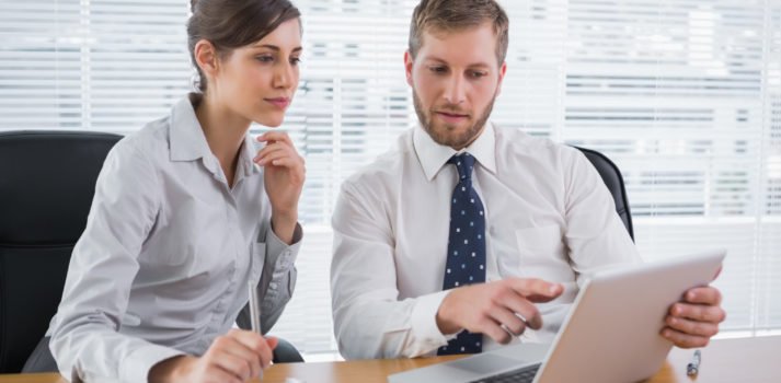 Mann in Businessoutfit erklärt Frau etwas am Laptop