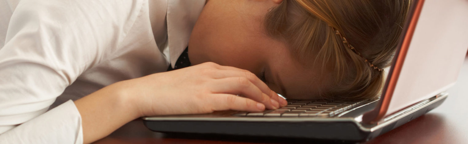 Frau liegt erschöpft mit ihrem Kopf auf ihrem Laptop