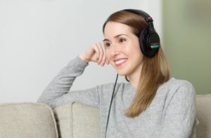 Frau sitzt lächelnd auf Sofa und hört Musik