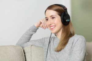 Frau sitzt lächelnd auf Sofa und hört Musik