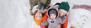 Familie liegt im Schnee, daneben liegt ein Schneemann
