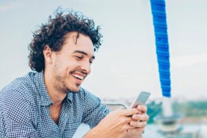 Mann sitzt auf Schiff und schaut ins Handy